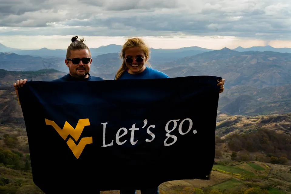 Daniel Brewster and another trip member holding a dark blue flag featuring the WVU logo that reads 'Let's go.'