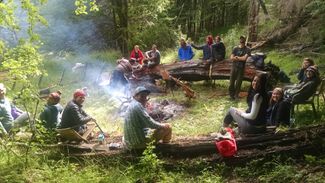 Students gathered around a day-time forest campfire