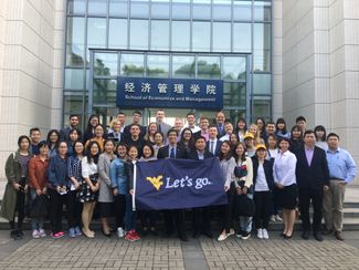 China Study Abroad group posing and holding a dark blue flag with the WVU logo that reads 'Let's go.'